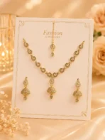Gold-tone jhumka necklace set with matching earrings and maang tikka displayed on cream fabric background