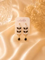 Gold-tone black and white crystal drop earrings displayed on satin fabric background