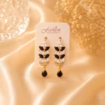Gold-tone black and white crystal drop earrings displayed on satin fabric background