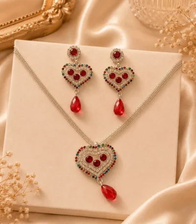 Silver-tone heart pendant necklace and matching red crystal earrings displayed on cream backdrop