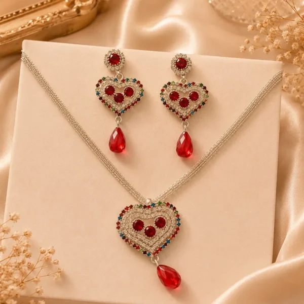Silver-tone heart pendant necklace and matching red crystal earrings displayed on cream backdrop